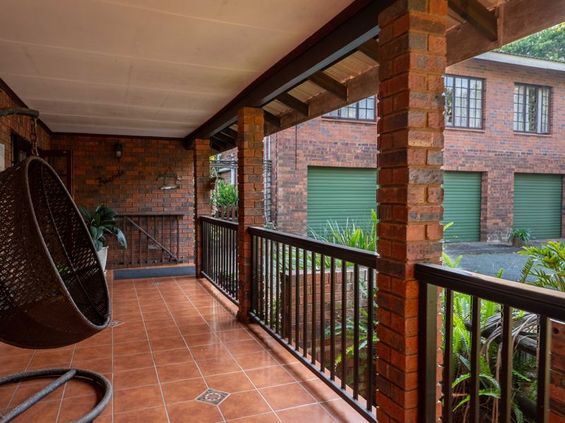 A covered brick patio featuring tiled flooring and a metal balustrade, overlooking the driveway and garage area.