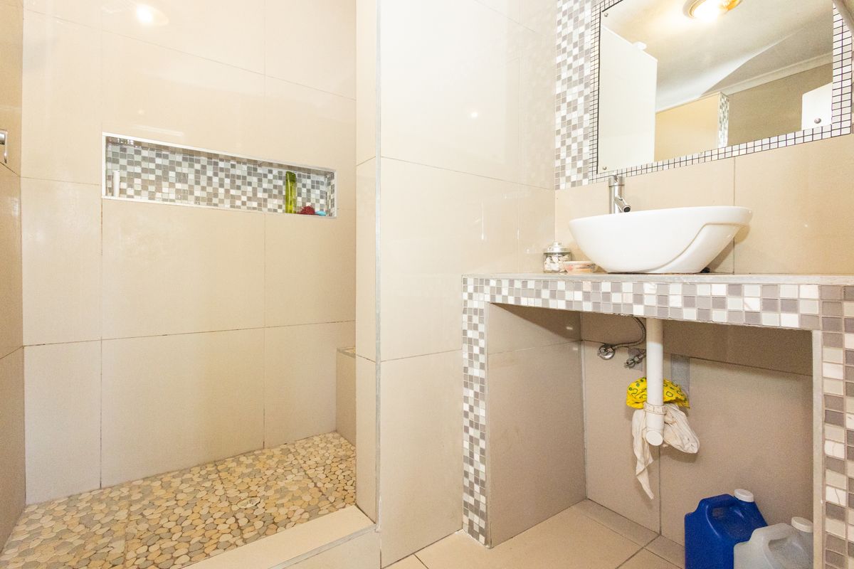 A bathroom featuring a tiled shower enclosure with a built-in niche and a vessel sink set on a mosaic-tiled vanity counter.