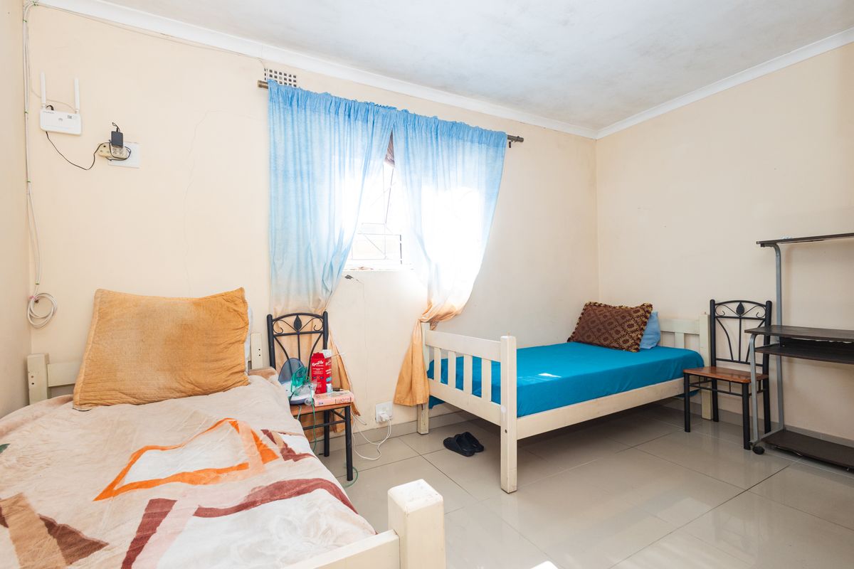 A bedroom featuring tiled flooring and coved ceilings, showing signs of wear including wall cracks and ceiling staining.