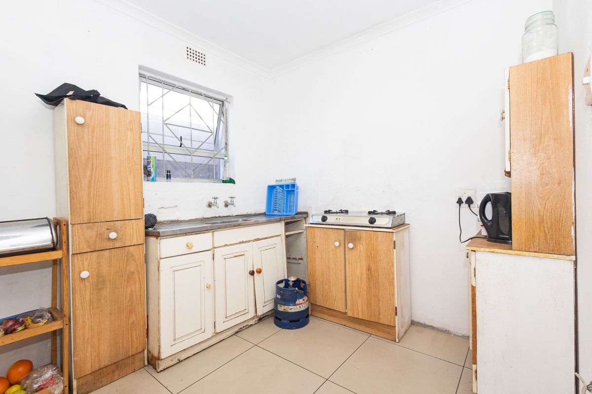 A compact kitchen featuring basic cabinetry, a stainless steel sink, tiled flooring, and a gas hob, requiring cosmetic updates and maintenance.