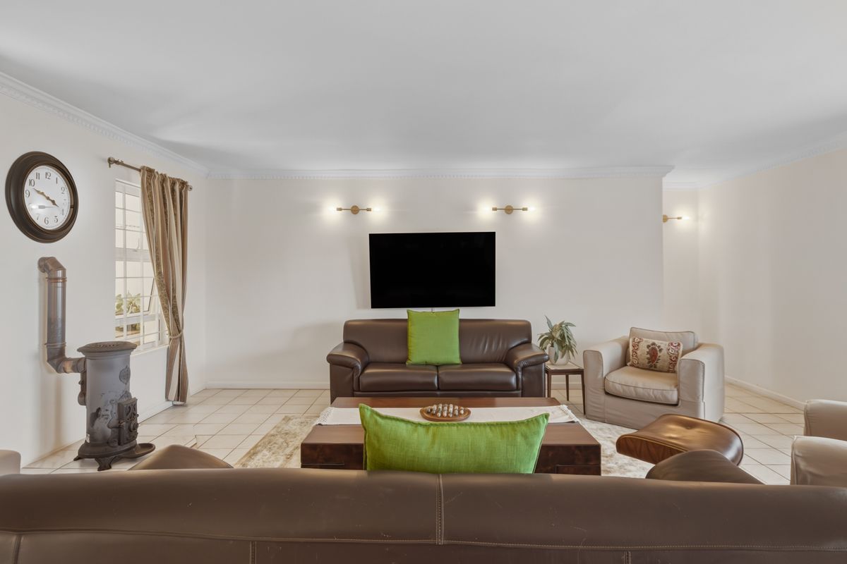 A spacious living room featuring tiled flooring, crown molding, wall-mounted lighting, and a classic cast iron fireplace.