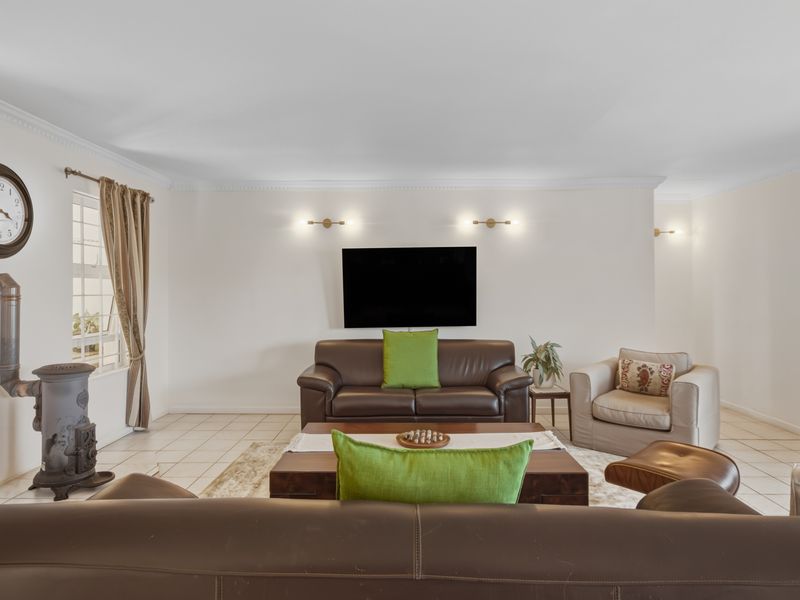 A spacious living room featuring tiled flooring, crown molding, wall-mounted lighting, and a classic cast iron fireplace.