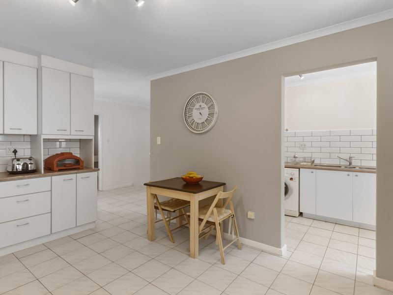 A clean, functional kitchen featuring white cabinetry, subway tile backsplash, and tiled flooring, with an adjacent scullery area for additional utility and storage.