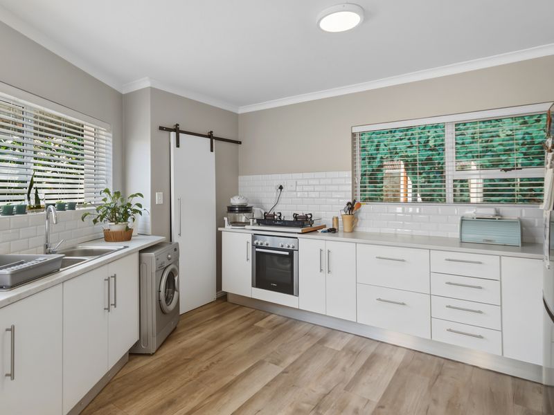 Modern kitchen featuring white cabinetry, subway tile backsplash, built-in oven with gas hob, double sink, and durable laminate flooring.