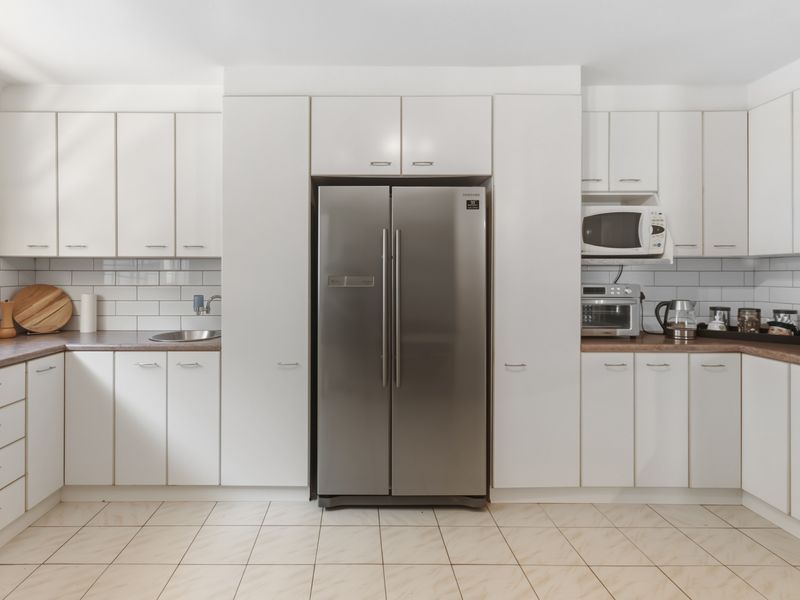 A clean, functional kitchen featuring white cabinetry, subway tile backsplash, laminate countertops, and a stainless steel refrigerator.