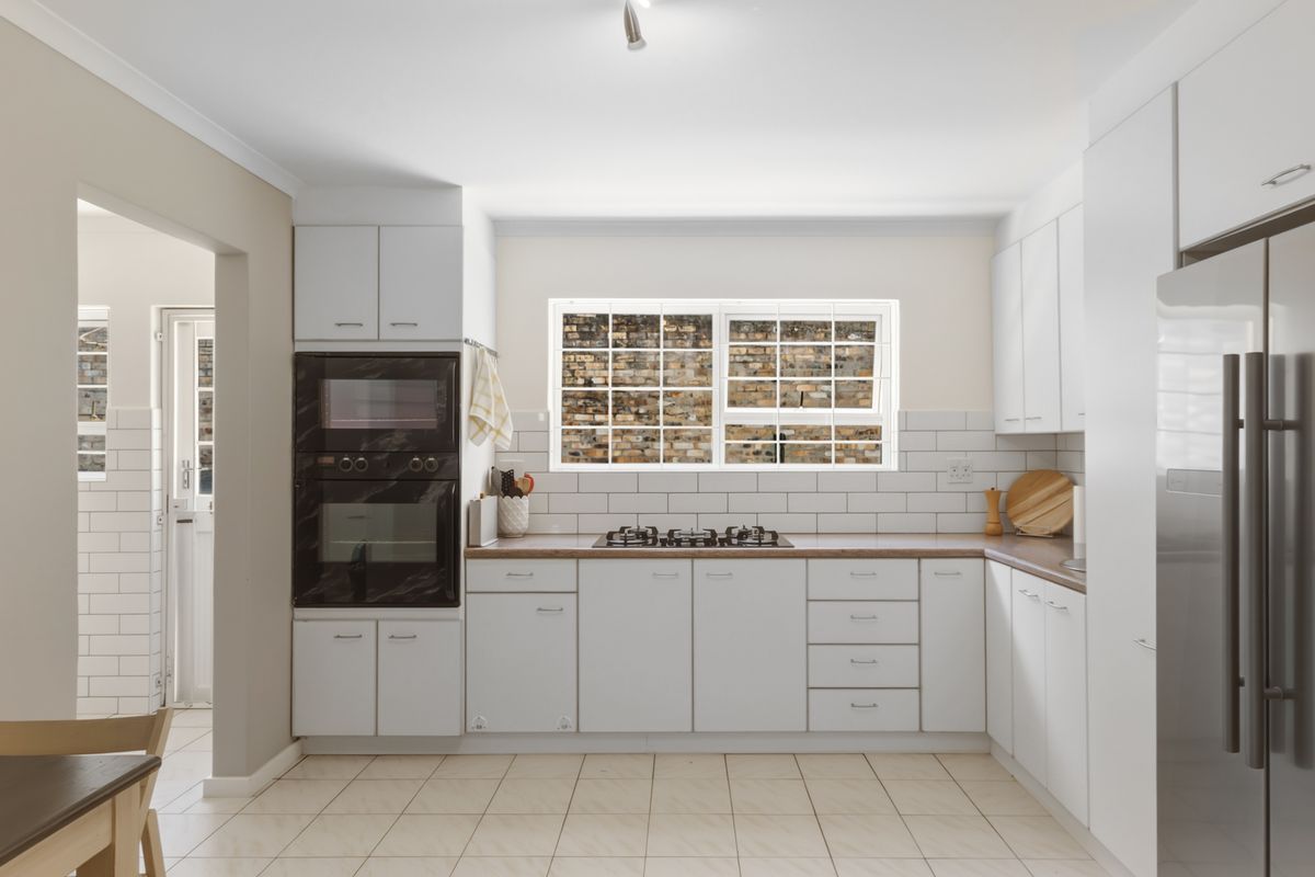 Modern kitchen featuring white cabinetry, subway tile backsplash, built-in oven and microwave, gas hob, and tiled flooring with a view to the rear exterior.