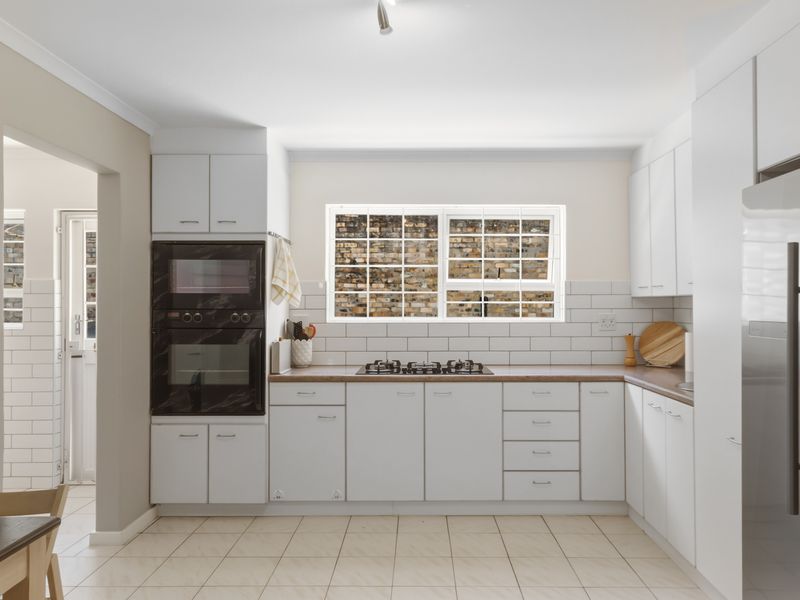 Modern kitchen featuring white cabinetry, subway tile backsplash, built-in oven and microwave, gas hob, and tiled flooring with a view to the rear exterior.