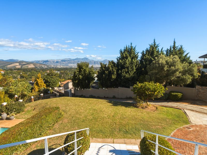 Elevated view overlooking a landscaped garden, swimming pool, and paved driveway with expansive mountain and valley vistas in the background.