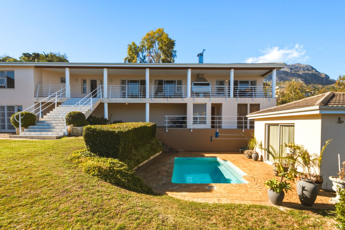 Rear view of the property featuring a swimming pool, brick paved patio, and a spacious covered balcony with built-in braai and mountain views.