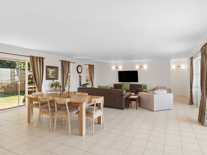 Spacious open-plan living and dining area featuring neutral tiled flooring, wall-mounted lighting, and large sliding glass doors providing access to the garden.