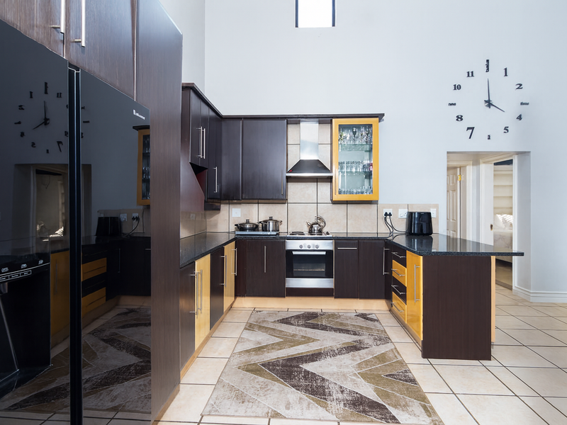 A spacious kitchen featuring dark wood cabinetry, granite countertops, stainless steel appliances, and high ceilings with tiled flooring throughout.