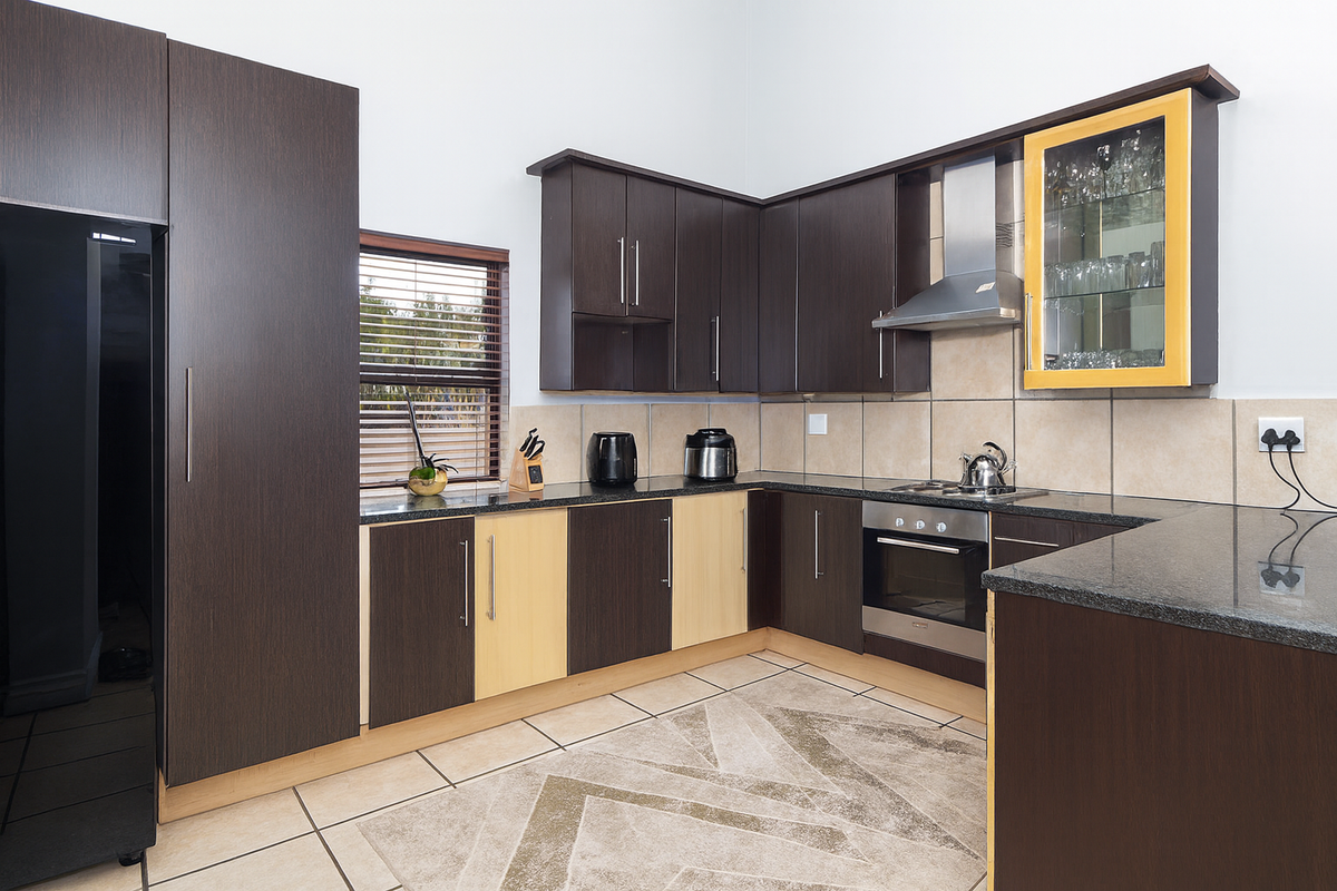 Modern kitchen featuring dark wood cabinetry, granite countertops, stainless steel appliances, and a tiled backsplash with a glass-fronted display cabinet.