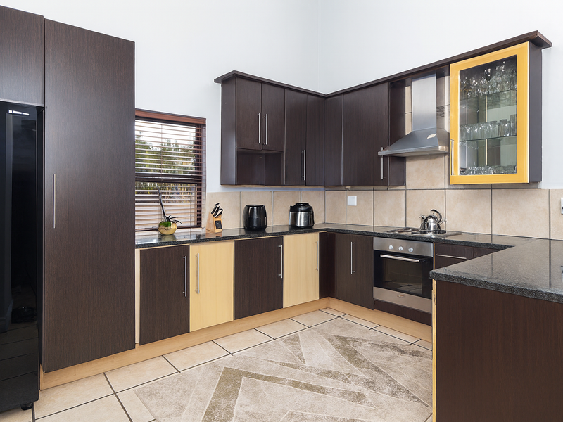Modern kitchen featuring dark wood cabinetry, granite countertops, stainless steel appliances, and a tiled backsplash with a glass-fronted display cabinet.