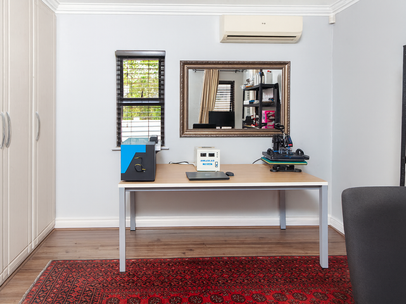 A functional home office featuring built-in storage cupboards, laminate flooring, and a wall-mounted air conditioning unit.