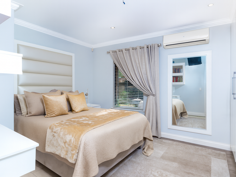 A well-maintained bedroom featuring a built-in headboard, integrated air conditioning, recessed lighting, and ample built-in wardrobe storage.