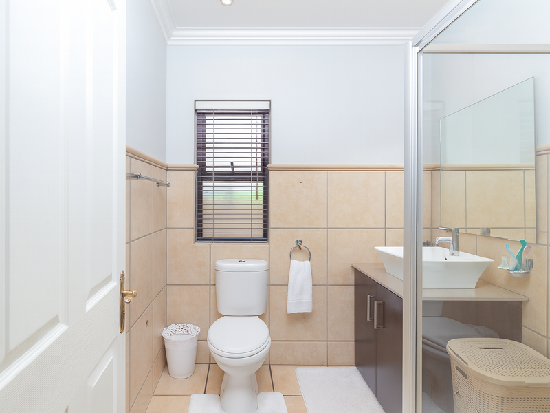 A clean, functional bathroom featuring a vessel sink vanity, a glass-enclosed shower, and neutral wall tiling with a window for natural light.