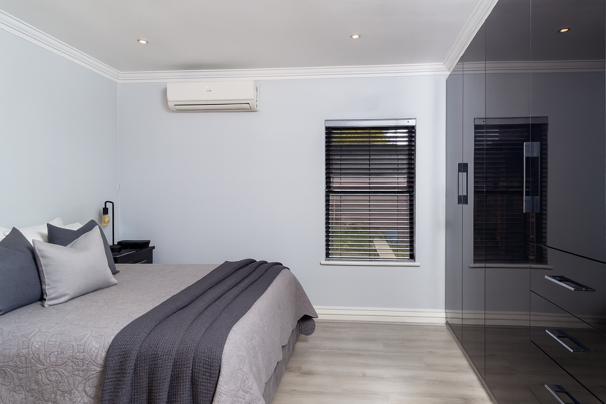 Modern bedroom featuring high-gloss built-in wardrobes, split-system air conditioning, recessed downlights, and neutral finishes with timber-look flooring.