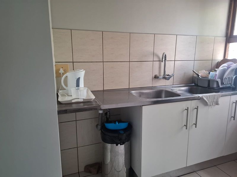 A functional kitchen area featuring a stainless steel double sink, tiled splashback, and built-in base cabinetry with laminate countertops.