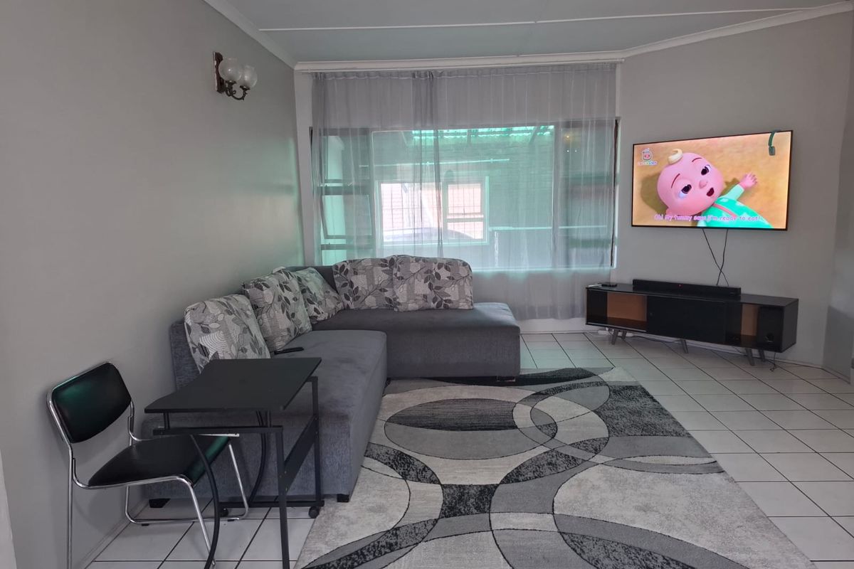 A living room featuring neutral wall tones, tiled flooring, and a large window, providing a functional and well-lit space for relaxation.