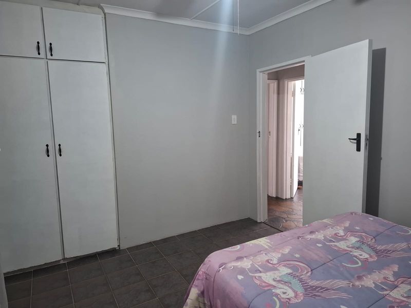 A bedroom featuring built-in cupboards, tiled flooring, and a ceiling fan, with a doorway leading to an adjacent hallway.