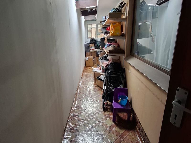 A narrow utility or storage corridor featuring tiled flooring, fixed shelving, and a skylight providing natural light.