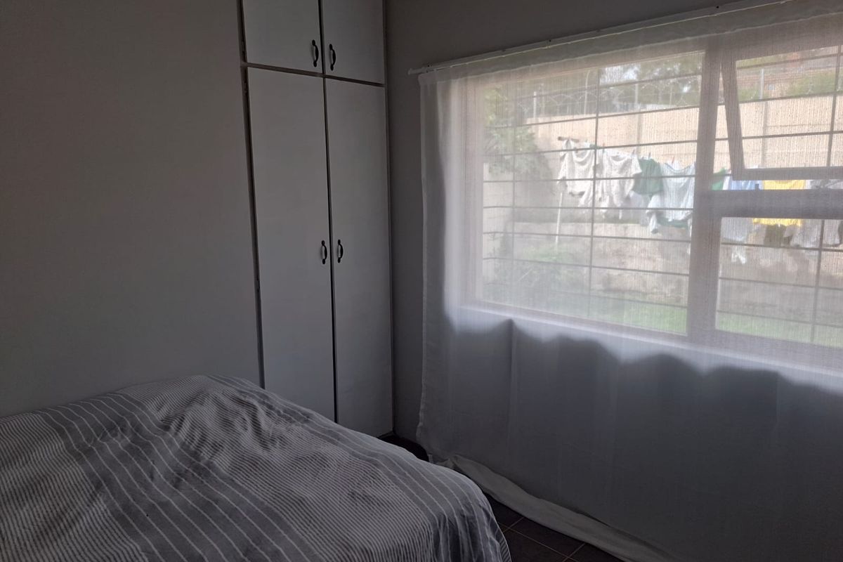 A bedroom featuring built-in cupboards, tiled flooring, and a window fitted with security bars.