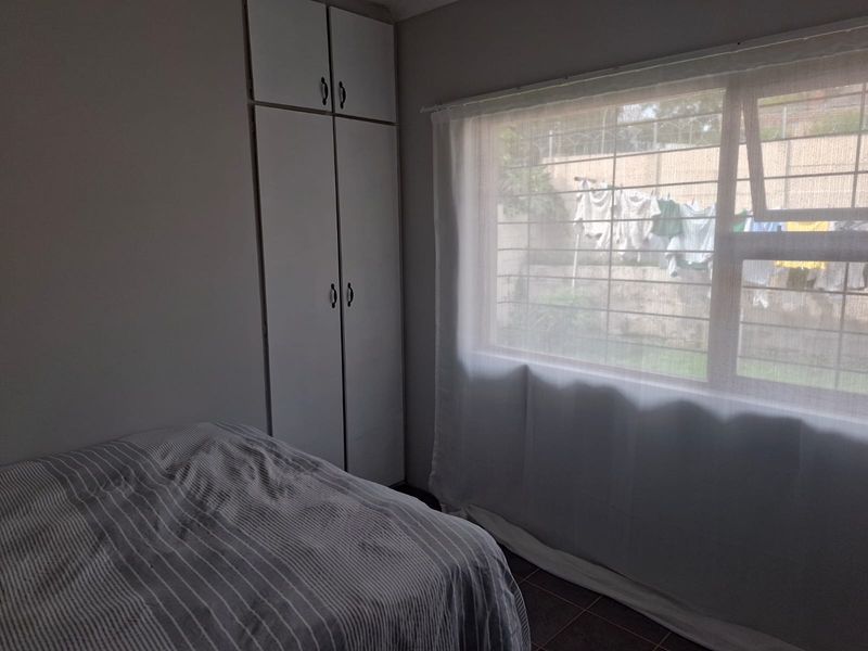 A bedroom featuring built-in cupboards, tiled flooring, and a window fitted with security bars.