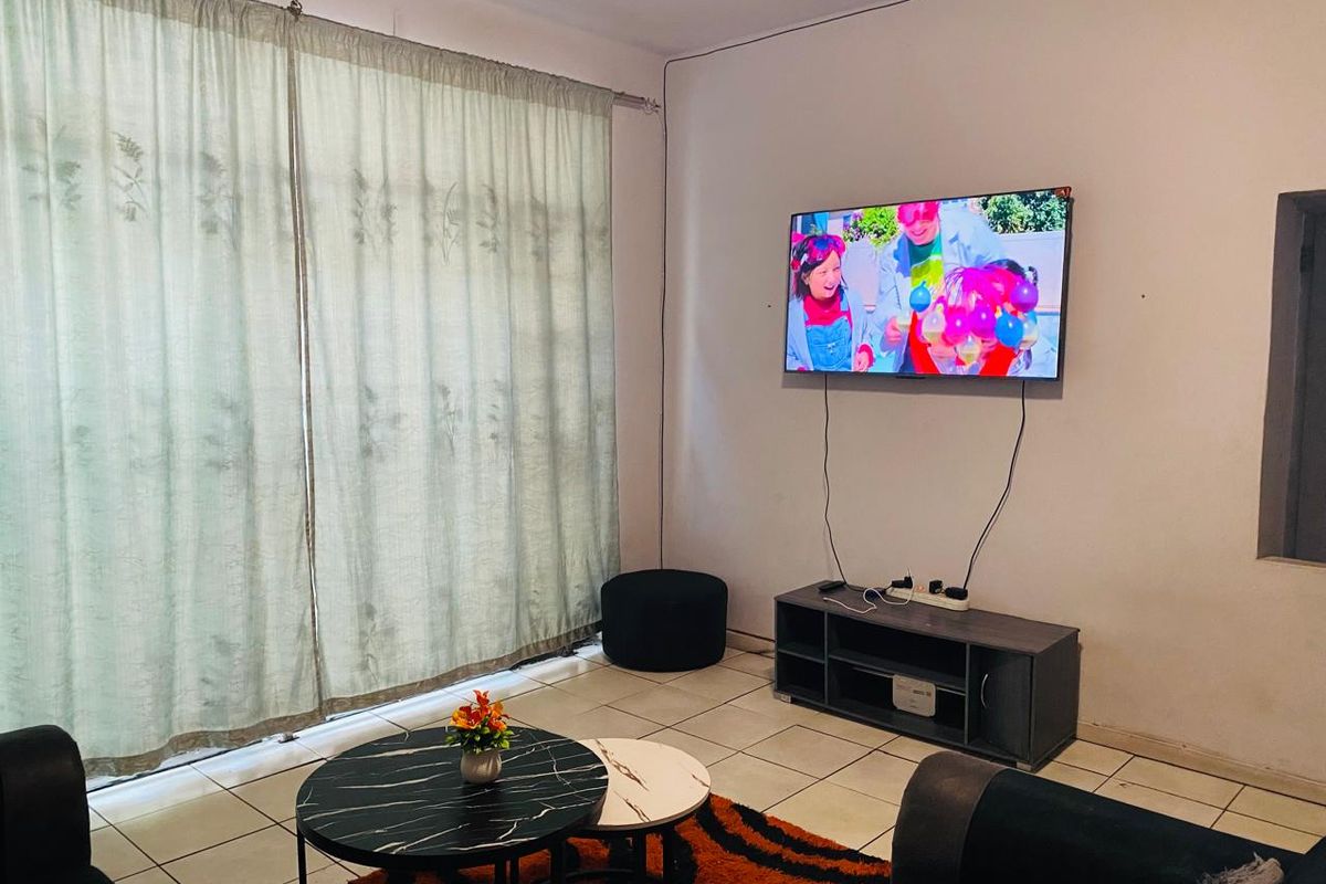 A living room area featuring tiled flooring and a large window with curtain rails, providing a functional space for relaxation.