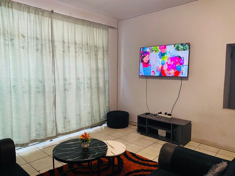 A living room area featuring tiled flooring and a large window with curtain rails, providing a functional space for relaxation.