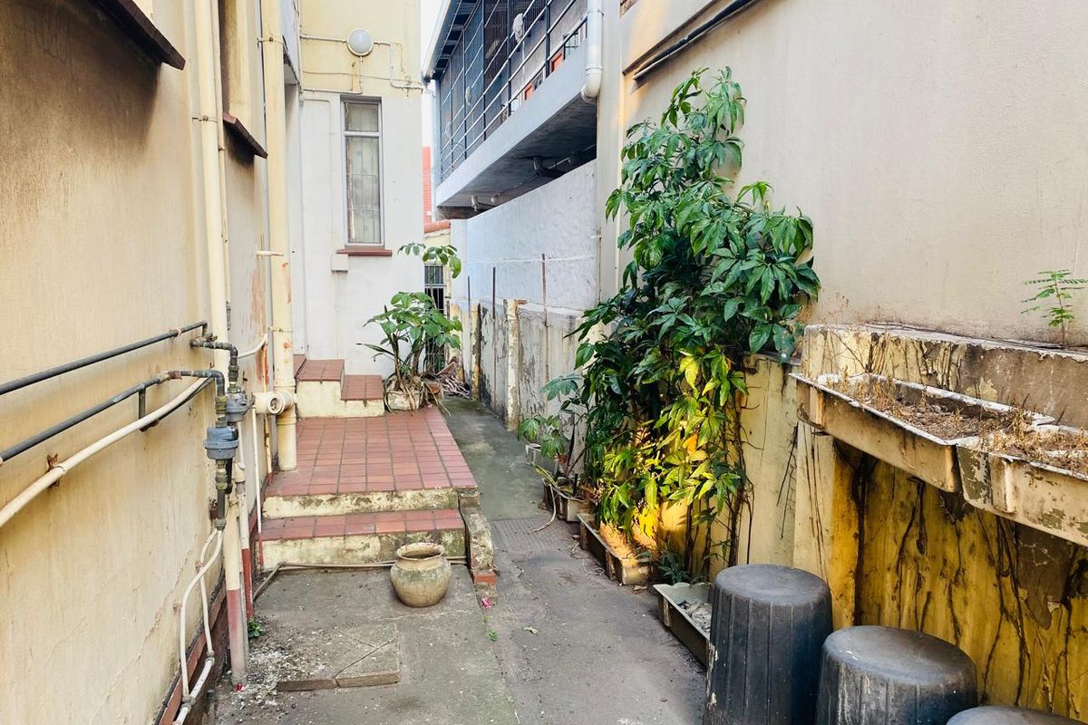 A narrow rear exterior passage featuring tiled steps, concrete pathways, and weathered masonry walls with integrated planter boxes.