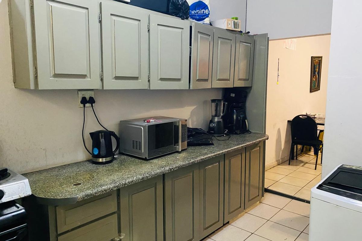 A functional kitchen featuring built-in cabinetry, granite countertops, and tiled flooring, providing a practical workspace with direct access to the adjacent living area.