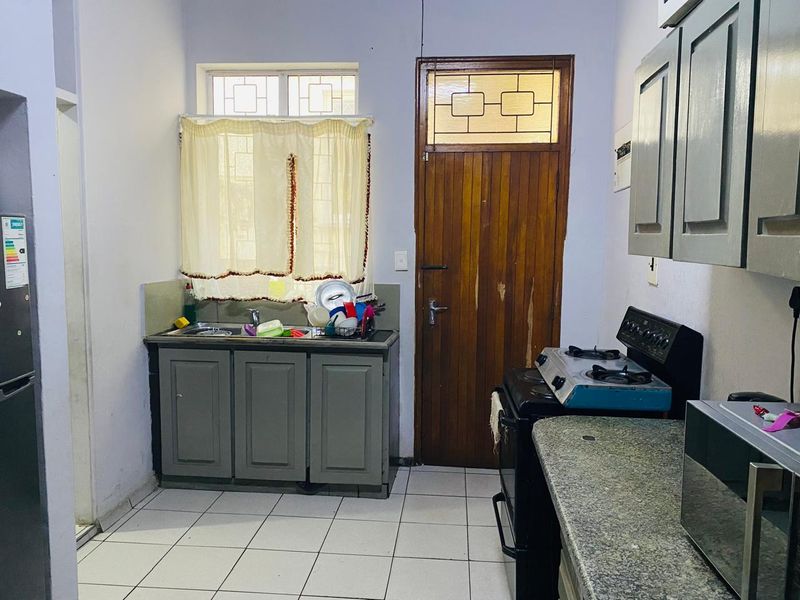 A functional kitchen featuring built-in cabinetry, stone countertops, tiled flooring, and a freestanding stove, with direct access to an exterior door.