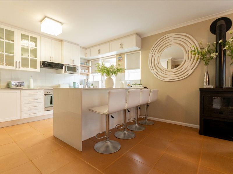 Modern kitchen featuring white cabinetry, a central island with breakfast bar seating, and a built-in wood-burning fireplace, finished with tiled flooring.