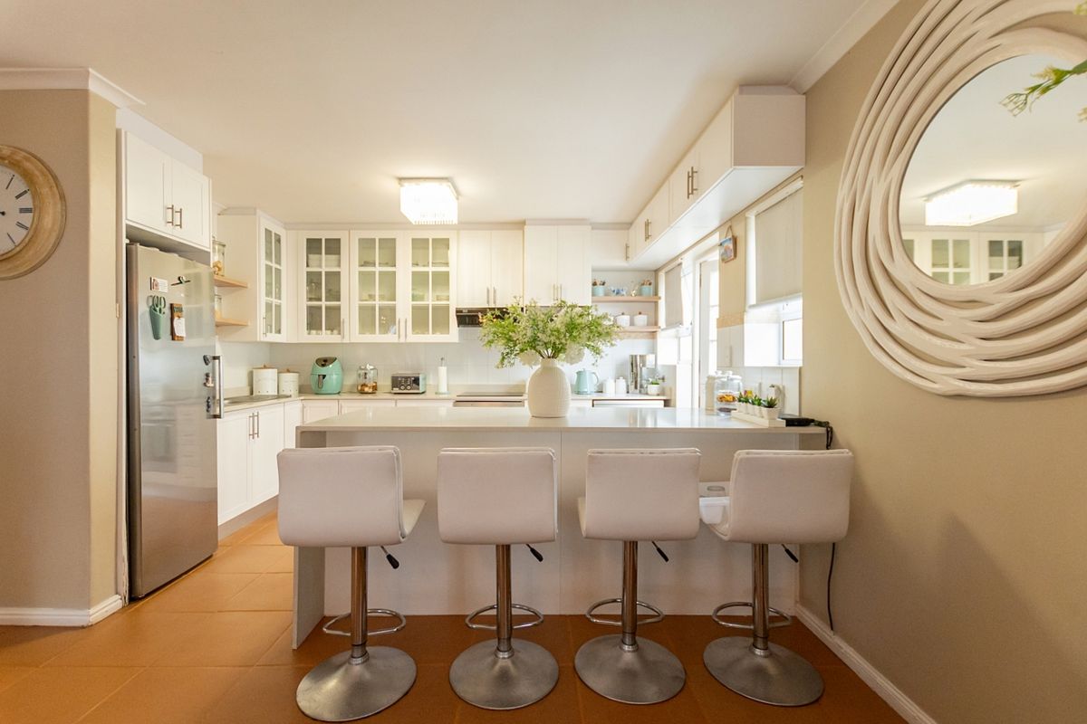 A bright, modern kitchen featuring white cabinetry, a central island with breakfast bar seating, and clean quartz countertops.