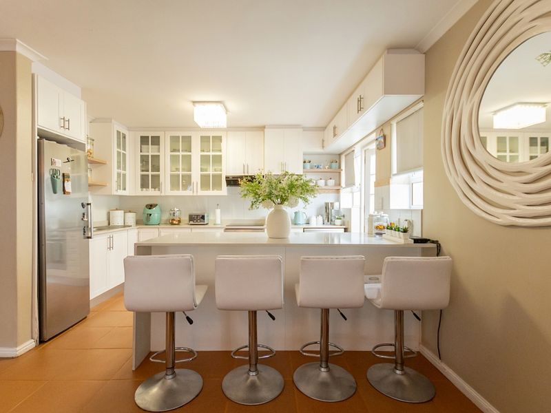 A bright, modern kitchen featuring white cabinetry, a central island with breakfast bar seating, and clean quartz countertops.