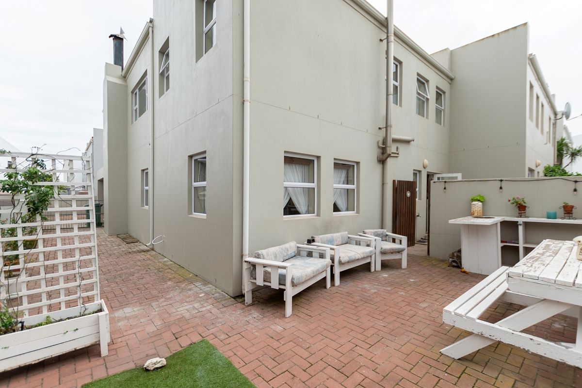 Rear exterior view of the property featuring a paved courtyard area with a built-in outdoor counter and trellis.