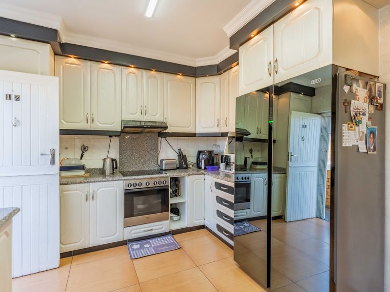 A functional kitchen featuring white cabinetry, granite countertops, built-in oven with hob, extractor fan, and tiled flooring with decorative cornice detailing.