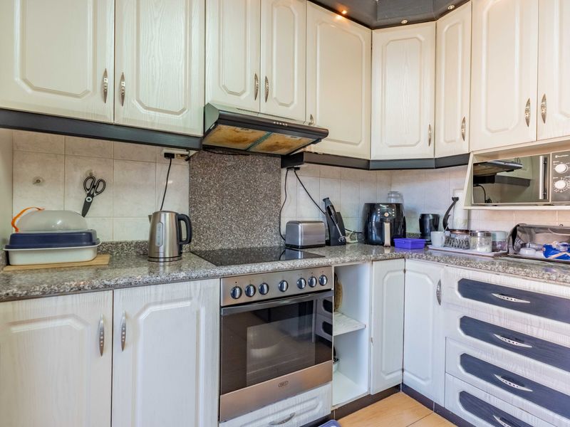 A functional kitchen featuring white cabinetry, granite countertops, a built-in oven with hob, and an extractor fan, offering a practical layout for daily cooking.