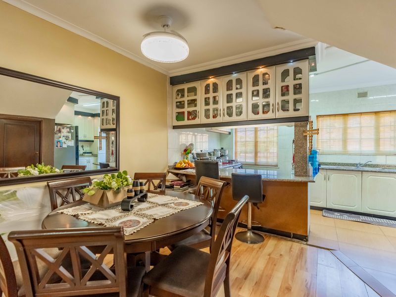 Open plan dining area flowing into a functional kitchen with granite countertops, breakfast bar, and ample built-in cabinetry.
