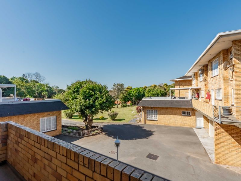 An elevated view of the townhouse complex courtyard featuring face brick buildings, an asphalt driveway, and landscaped garden areas.