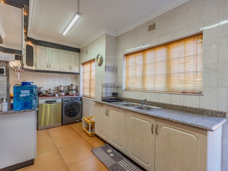 A functional kitchen featuring built-in cabinetry, laminate countertops, a double stainless steel sink, and tiled finishes, offering a practical layout for daily use.
