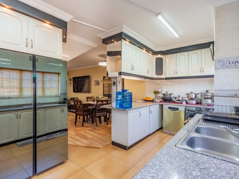 Open plan kitchen featuring granite countertops, ample built-in cabinetry, and a double basin sink, seamlessly flowing into the adjacent dining and living area.