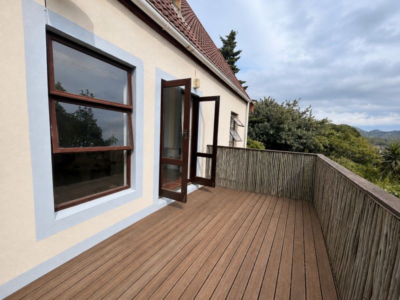 A spacious elevated balcony featuring timber decking and a natural timber balustrade, offering direct access to the interior through french doors.