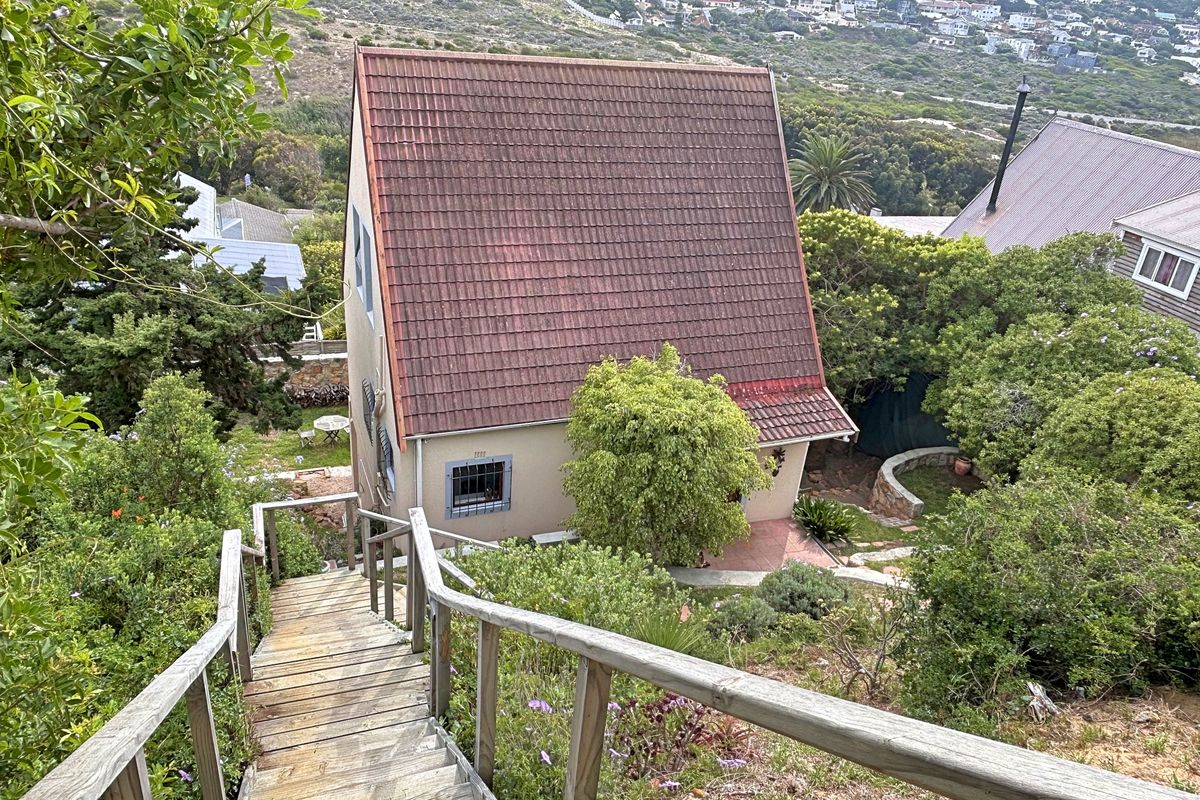 Elevated view of a residential property featuring a steep tiled roof, surrounded by lush garden landscaping and accessed via a wooden staircase.
