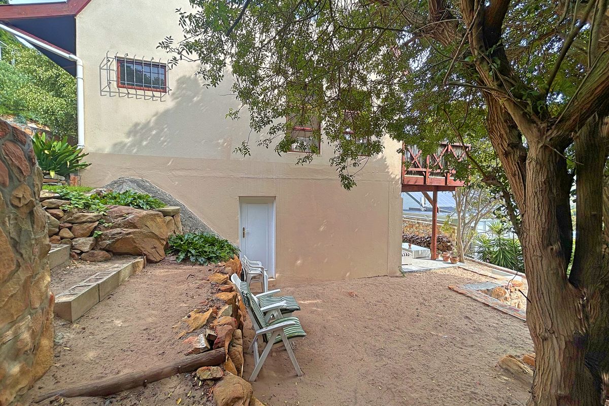 Rear exterior view of the property featuring a stone retaining wall, sandy garden area, and a raised timber balcony.