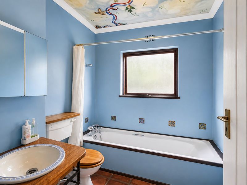 A bathroom featuring a built-in bathtub, wooden vanity with basin, and a unique decorative ceiling mural, finished with terracotta floor tiles.