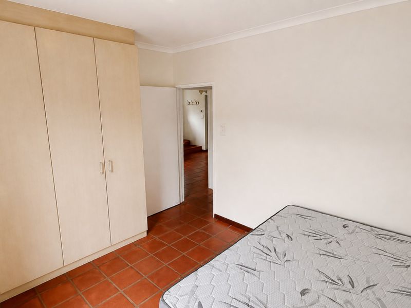 Bedroom featuring built-in cupboards and terracotta floor tiles, offering a functional space with neutral wall finishes.
