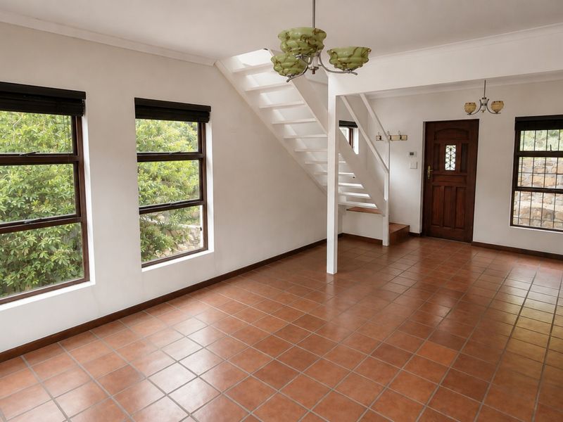 A bright and spacious entrance area featuring terracotta tiled flooring, a central staircase, and large windows providing ample natural light.
