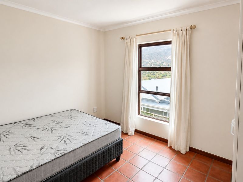 A bright, empty bedroom featuring terracotta floor tiles, a built-in wardrobe, and a window with views of the surrounding landscape.
