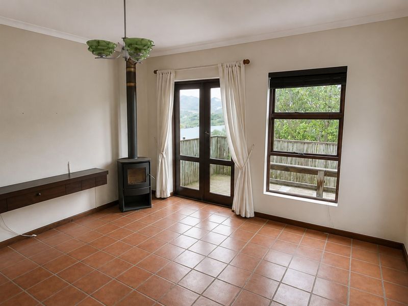 A bright, empty living room featuring terracotta tiled floors, a freestanding fireplace, and direct access to an outdoor deck through double glass doors.